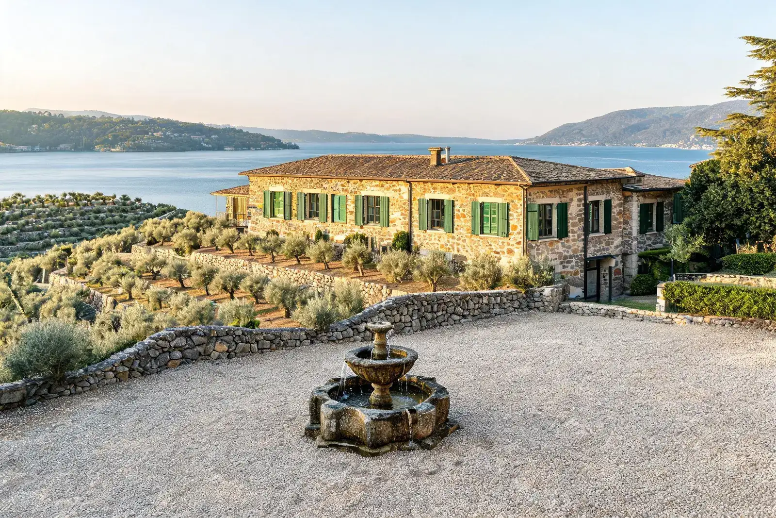 Residenza Oliveto a Brissago: casa in granito con persiane verdi in un uliveto terrazzato, corte in ghiaia con una fontana in pietra.